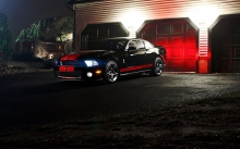 Черный Ford Mustang Shelby с красными полосами у въезда в гараж